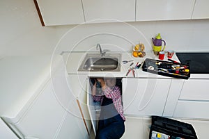 Handyman Lying On Floor Repairing Sink In Kitchen