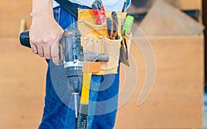 Handyman manual worker in tools belt and holding drill in his hands, Carpenter working with equipment in wood workshop, man doing