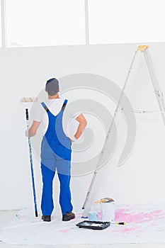 Handyman with paint roller examining wall at home