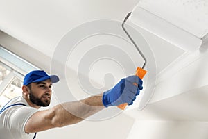 Handyman painting ceiling with white dye, focus on roller