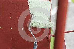 A handyman paints old glider swing made of wrought iron with red oxide primer paint.