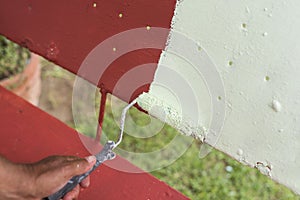 A handyman paints old glider swing made of wrought iron with red oxide primer paint.