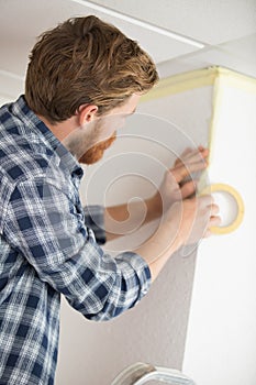 handyman prepares walls for painting with masking tape