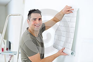 Handyman putting up wallpaper on white walls