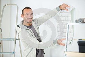 Handyman putting up wallpaper on white walls