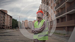 A handyman in a reflective vest, helmet, and safety glasses with his hands on his chest proudly inspects the houses as