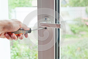 Handyman repairs plastic window with screwdriver. Workman adjusts the operation of the plastic window