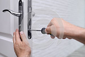 Handyman with screwdriver repairing door lock, closeup