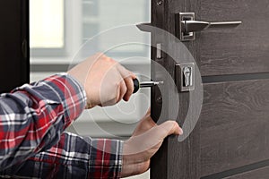 Handyman with screwdriver repairing door lock indoors, closeup