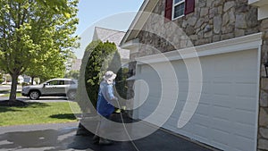 A handyman is seen washing down a white garage door and the stone front of a house