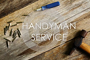 Handyman service written on wooden background with screwdriver and hammer