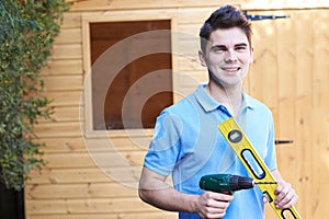 Handyman Standing Outside Garden Shed With Tools