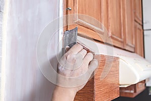 A handyman using a piece of sandpaper to smoothen out the edge of a wall cabinet prior to painting. Home renovation or finishing photo