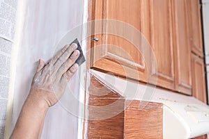 A handyman using a piece of sandpaper to smoothen out the edge of a wall cabinet prior to painting. Home renovation or finishing photo
