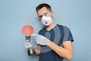 Handyman wearing respirator grinding wall with disc sanding machine. Worker labor and business concept