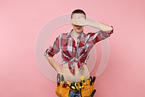 Handyman woman in shirt, denim shorts, kit tools belt full of variety useful instruments cover eyes with hand isolated