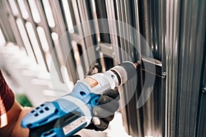 Handyman worker using electrical cord screwdriver for fastening screws into metal fence photo