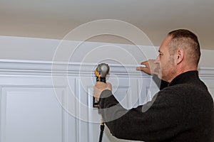 Handyman working using brad nail gun to Crown Moulding on white wall cabinets framing trim,