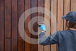 Handywoman applying protective varnish or paint with brush on wood fence wall cladding