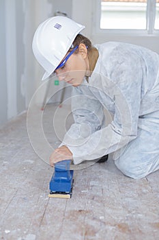 handywoman sanding wooden floor in construction site