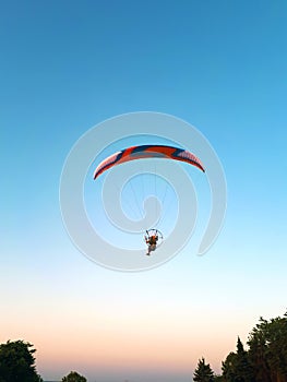 A hang-glider with a motor flies against a blue sky