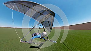 Hang glider pilot approaches landing on the green grassy field photo