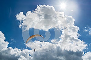 Hang glider riding upwards to reach clouds under the sun