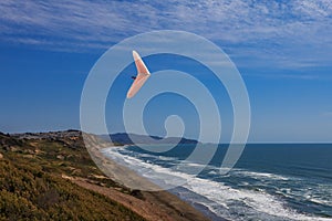 Hang gliding man flying above ground and ocean on a white wing a