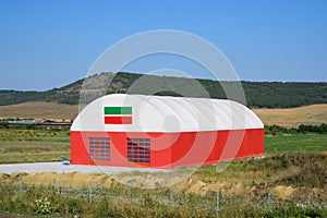 The hangar is white and red. An hangar in field