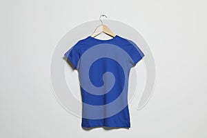 Hanger with blue t-shirt on light wall. Mockup for design