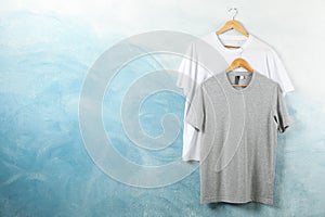 Hangers with blank white and gray t-shirts on blue background