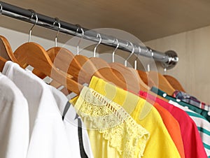 Hangers with bright clothes on rack in wardrobe