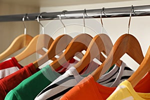 Hangers with bright clothes on rack in wardrobe, closeup