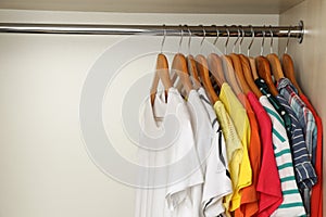 Hangers with bright clothes on rack in wardrobe, space for text