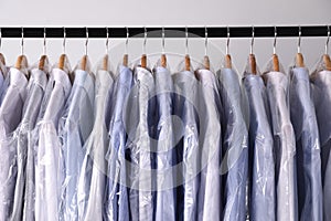 Hangers with shirts in dry cleaning plastic bags on rack against light background