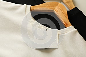 Hangers with stylish sweatshirts and blank tag, close up