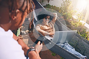 Hanging around online and outside. a young woman using a laptop and relaxing on a hammock while her boyfriend uses a