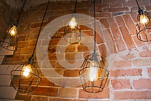 hanging from the ceiling are a few light bulbs in a minimal black lattice metal shade against a brick wall