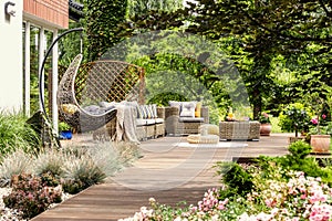 Hanging chair and pouf on wooden veranda in the middle of garden