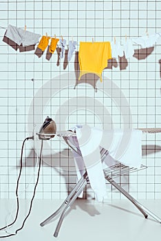 hanging clothes and ironing board with white tile on background