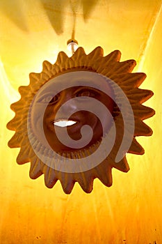 Hanging decoration of a smiling terra cotta sunshine with bright orange-yellow background