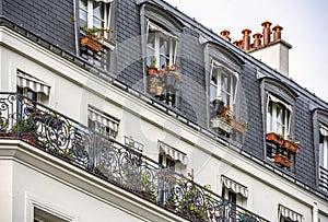 Hanging flower pots in the windows of the attic floor and on the balcony of multistory apartment building with textile sunshades