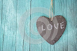 Hanging heart and turquoise wooden background in country style.