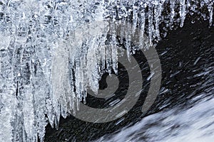 Hanging icicles above streaming water in winter