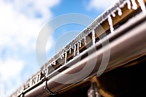 Hanging icicles from the roof of a wooden building on a winter frosty day, a lot of snow on the roof, a visible plastic gutter and