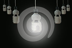 Hanging light bulbs with glowing one on dark background.