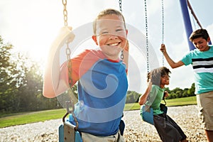 Hanging out with my best buddies. Portrait of a young boy playing on a swing at the park with his friends.