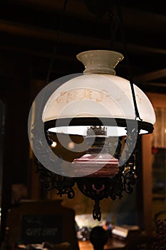 Hanging pendant light in shape of vintage kerosene lamp with matte white glass lampshade globe on dark blurred background.