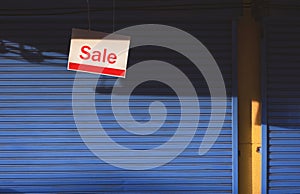 Hanging sale sign board in front of blue automatic shutter door of shop house