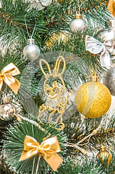 Hanging squirrel figure decoration on the Christmas tree. Gold and silver baubles, multi-colored bows, bells, lit garlands against